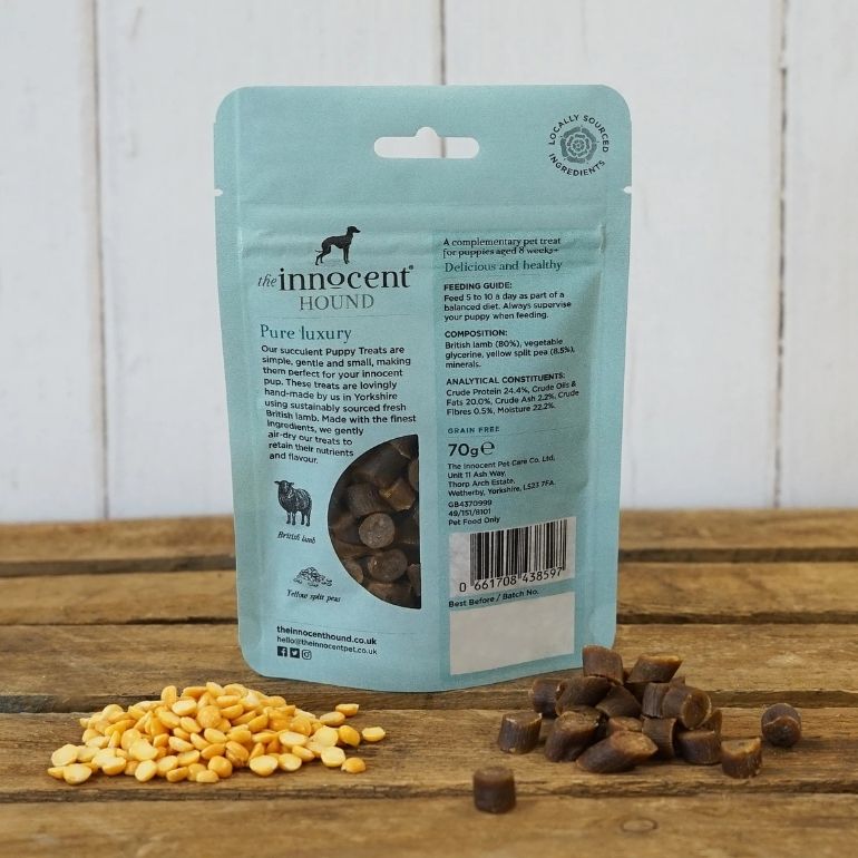 Bilde av baksider av en pose The Innocent Hound Puppy Training Treats. Pakken står på et bord omgitt av godbiter og erter.
